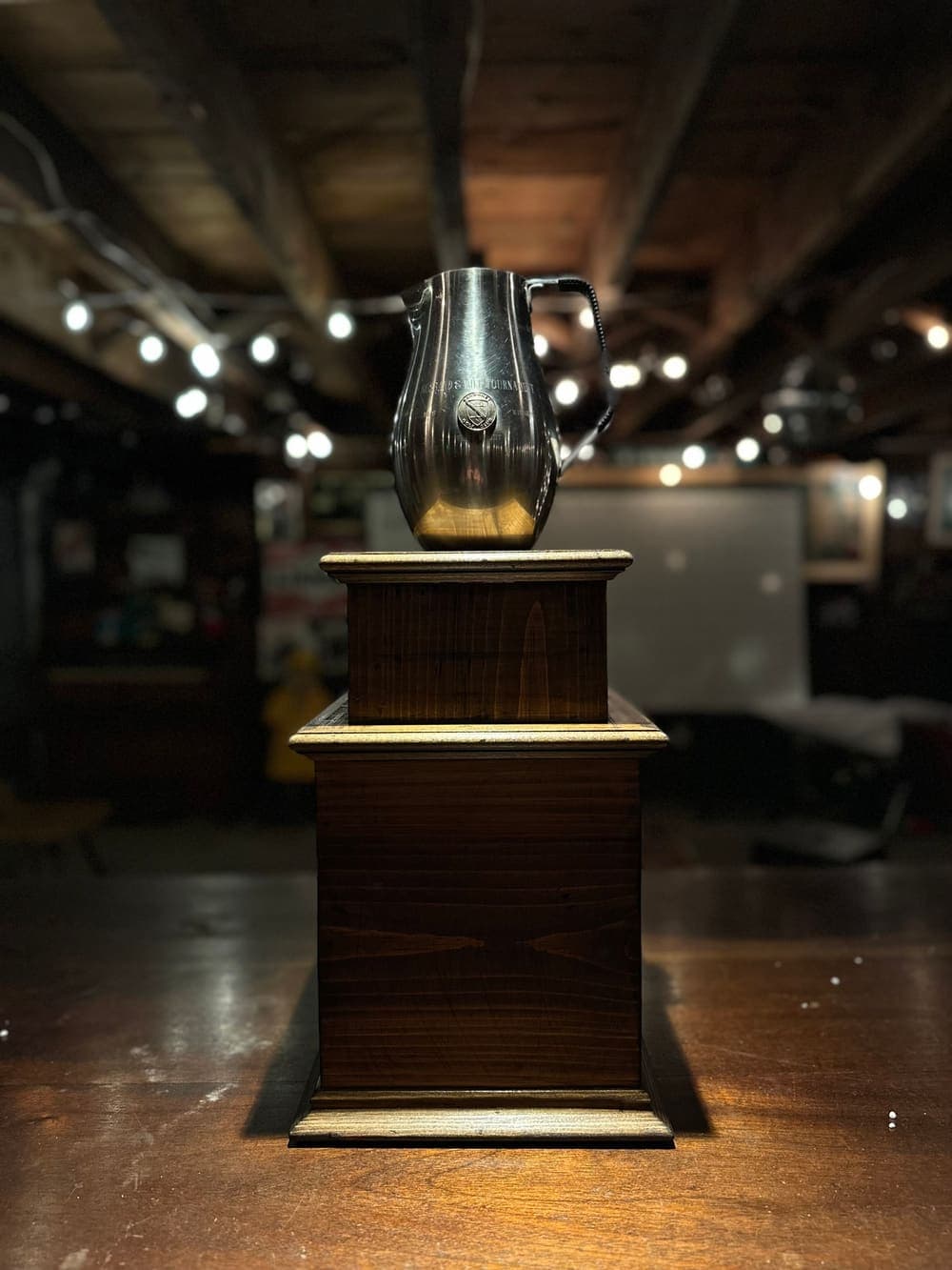 The Gimme Cup: the pewter pitcher on its wooden pedestal, under the basement lights